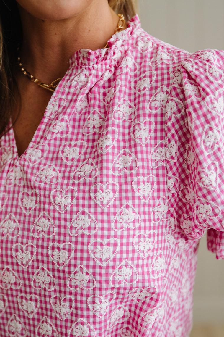 Close-up of a person wearing a pink and white checkered blouse with floral patterns.