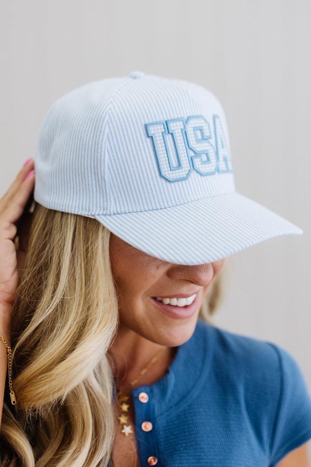 Woman wearing a blue and white striped cap with 'USA' on it, smiling against a neutral background