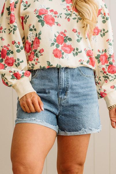 Person wearing a floral blouse and denim shorts against a neutral background