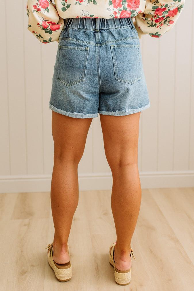 Person wearing denim shorts and a floral blouse in a neutral setting