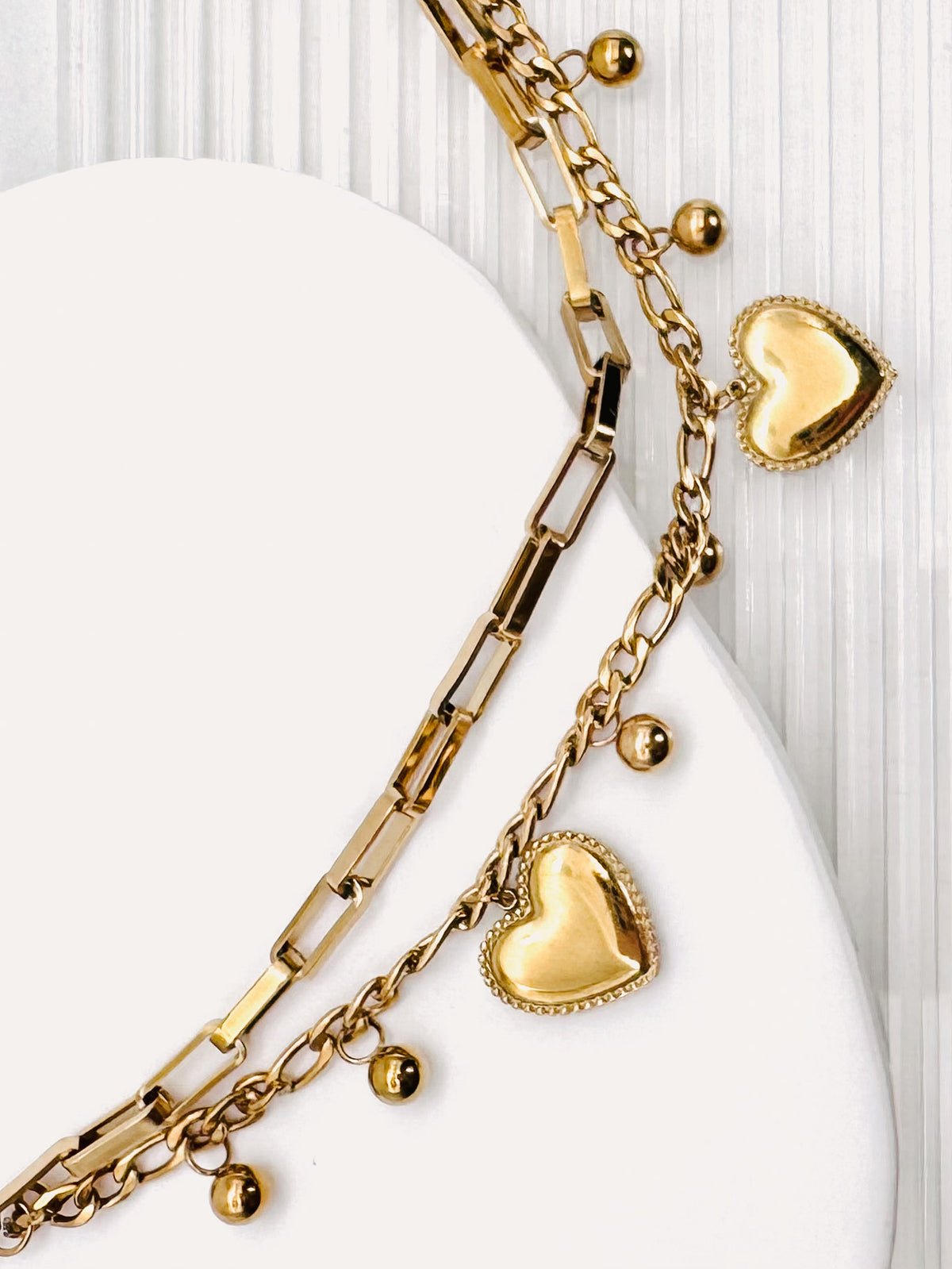 Close up of a 18k Gold Plated Waterproof Stainless Steel Bracelet with Heart and dot charms on a white stone surface.