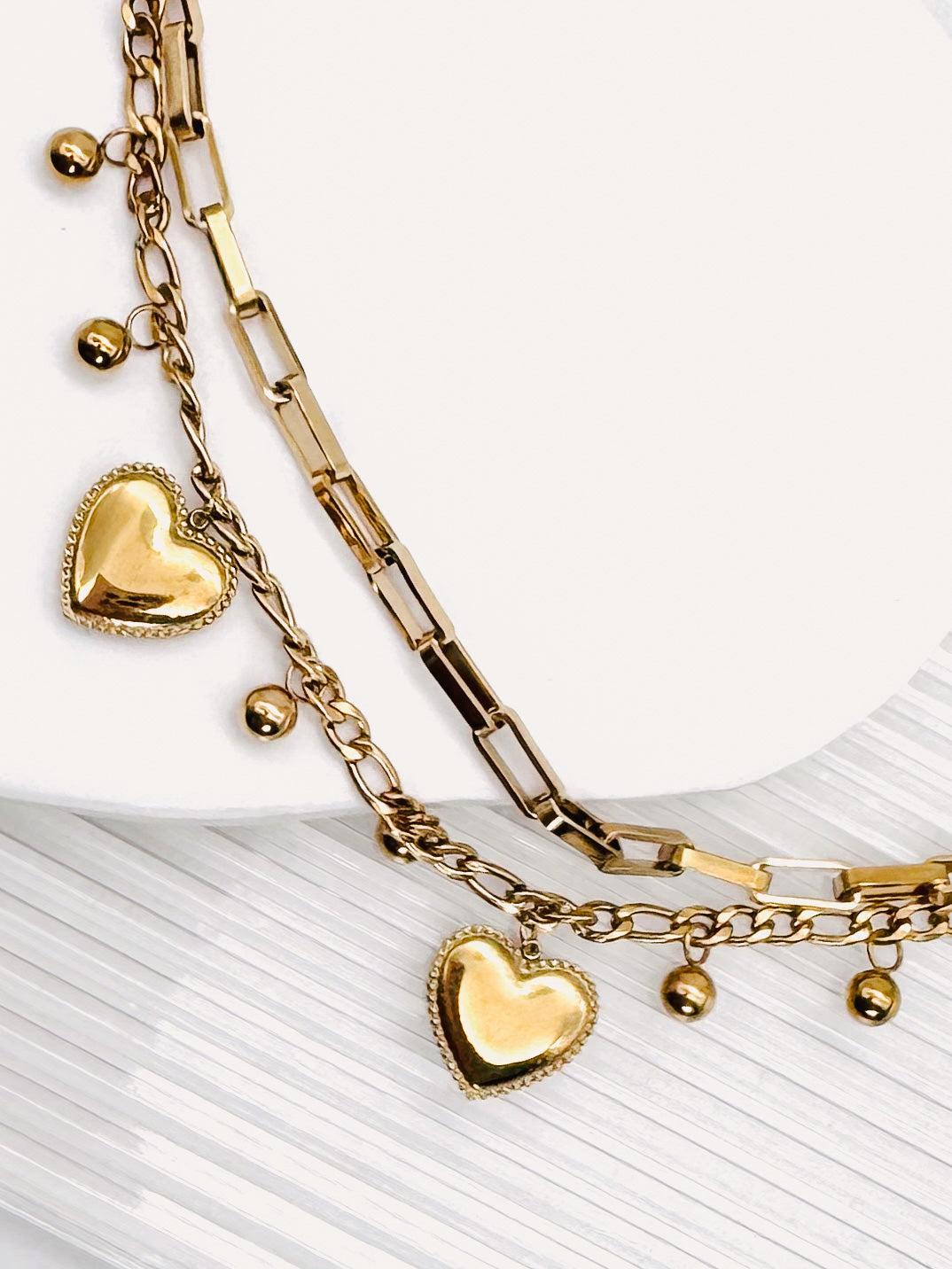 Close up of a 18k Gold Plated Waterproof Stainless Steel Bracelet with Heart and dot charms on a white stone surface.