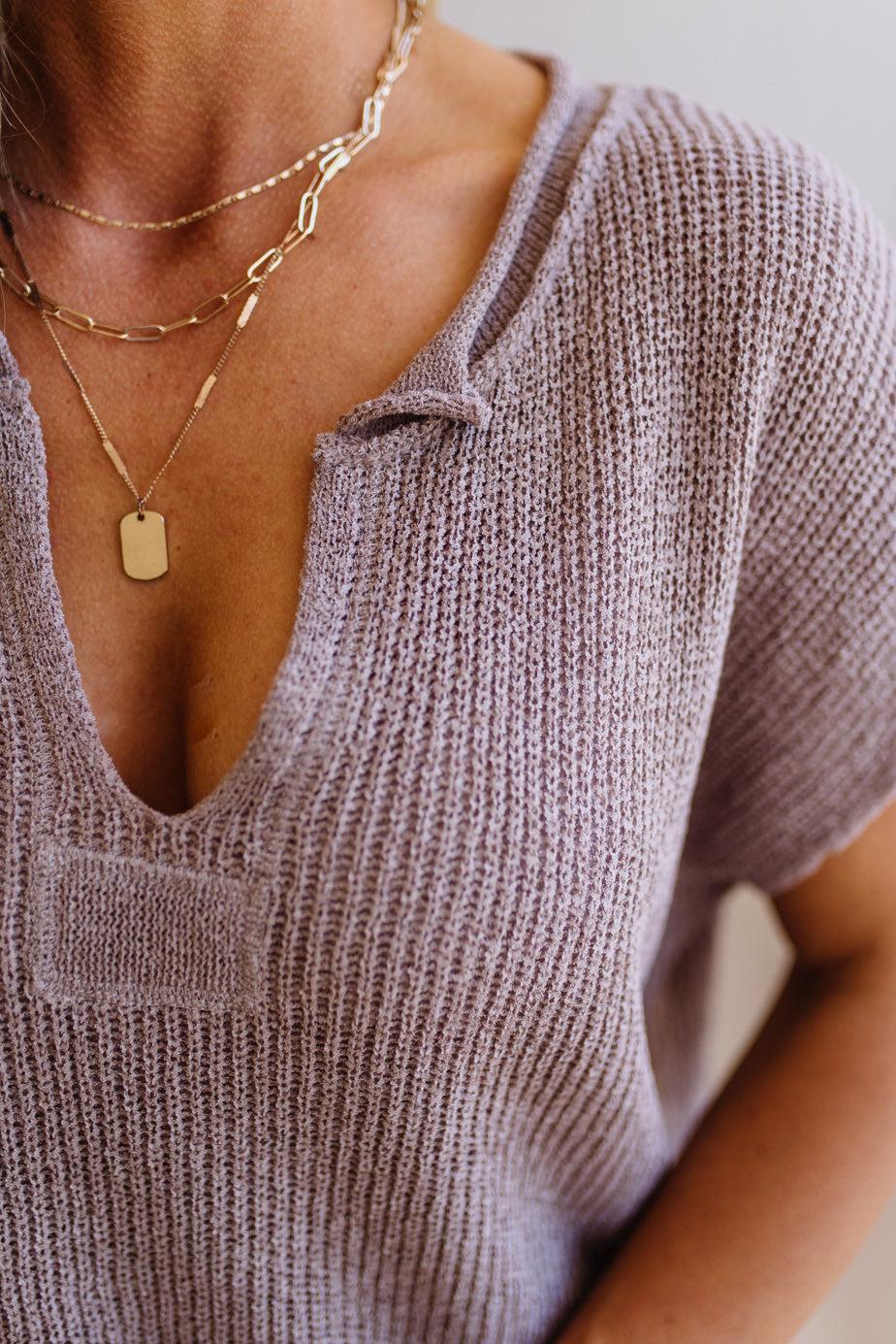 Blonde woman wearing a short sleeve v-neck ribbed texture sweater with center patch accent in mocha.