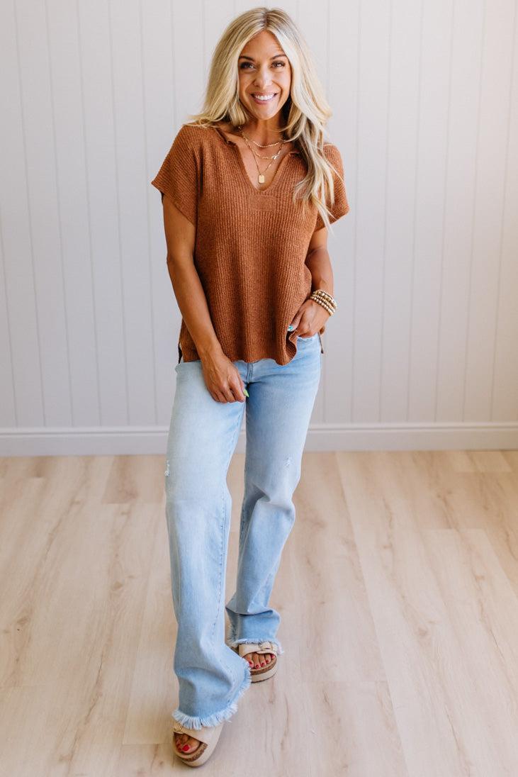 Blonde woman wearing a short sleeve v-neck ribbed texture sweater with center patch accent in rust.
