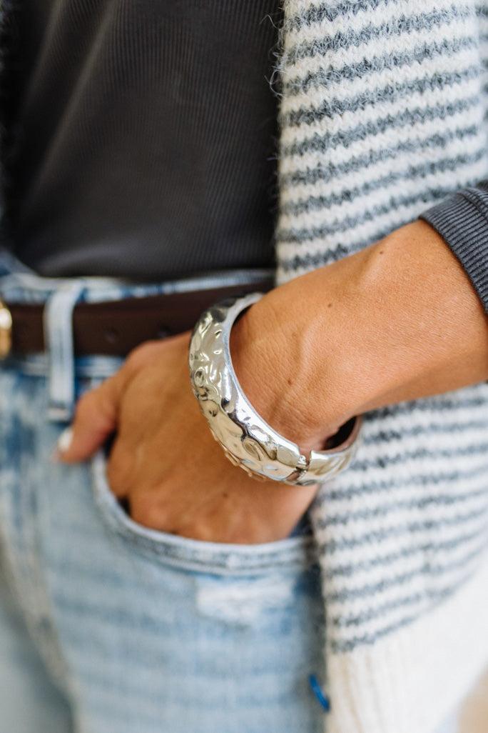 Woman in striped top and light jeans with her hand an a pocket and focused on a large silver bangle.