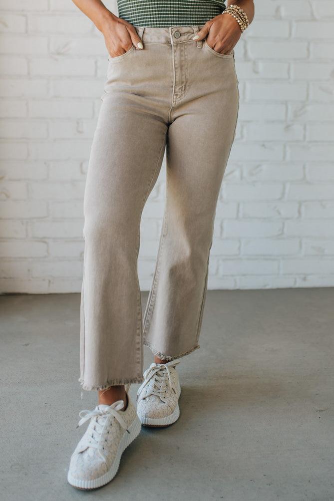 Blonde woman wearing ash mocha colored solid stretch jeans with mid rise and wide leg and a distressed hem accent.