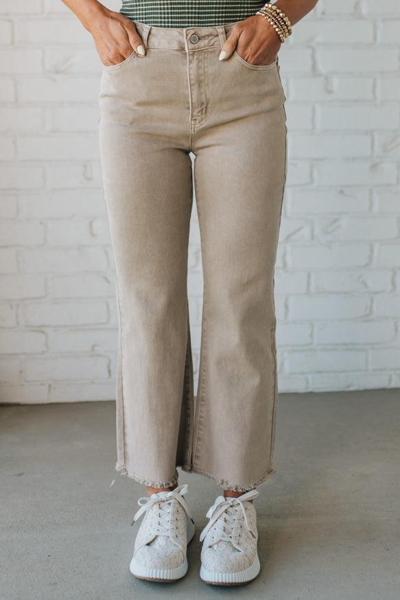 Blonde woman wearing ash mocha colored solid stretch jeans with mid rise and wide leg and a distressed hem accent.
