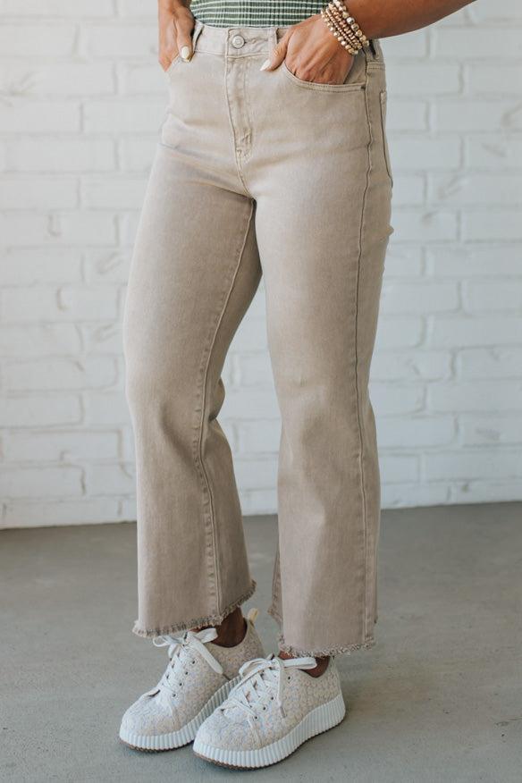 Blonde woman wearing ash mocha colored solid stretch jeans with mid rise and wide leg and a distressed hem accent.