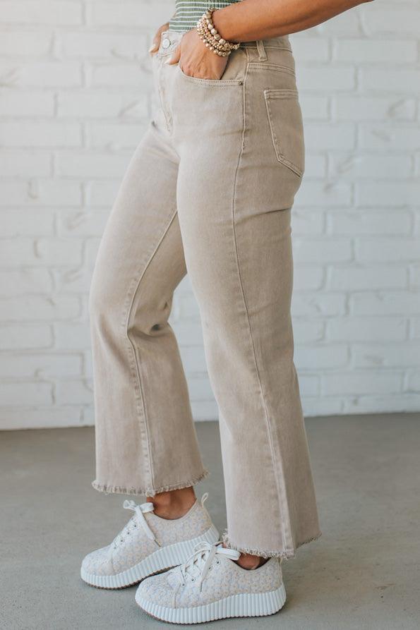Blonde woman wearing ash mocha colored solid stretch jeans with mid rise and wide leg and a distressed hem accent.