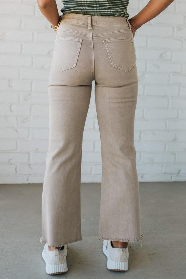 Blonde woman wearing ash mocha colored solid stretch jeans with mid rise and wide leg and a distressed hem accent.