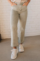Blonde woman wearing light olive acid wash crop jeans with frayed ankle.
