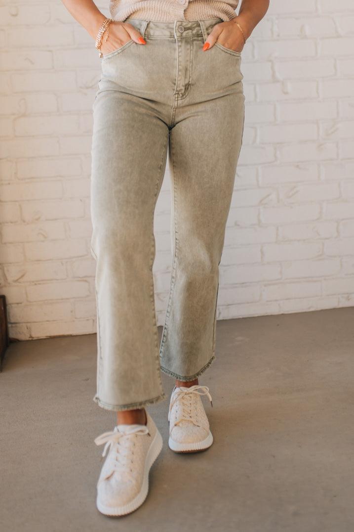 Blonde woman wearing light olive acid wash crop jeans with frayed ankle.