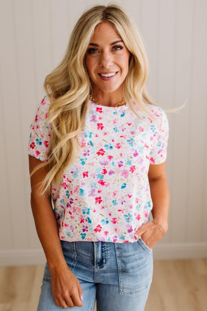 Woman wearing a colorful floral top and jeans against a neutral background