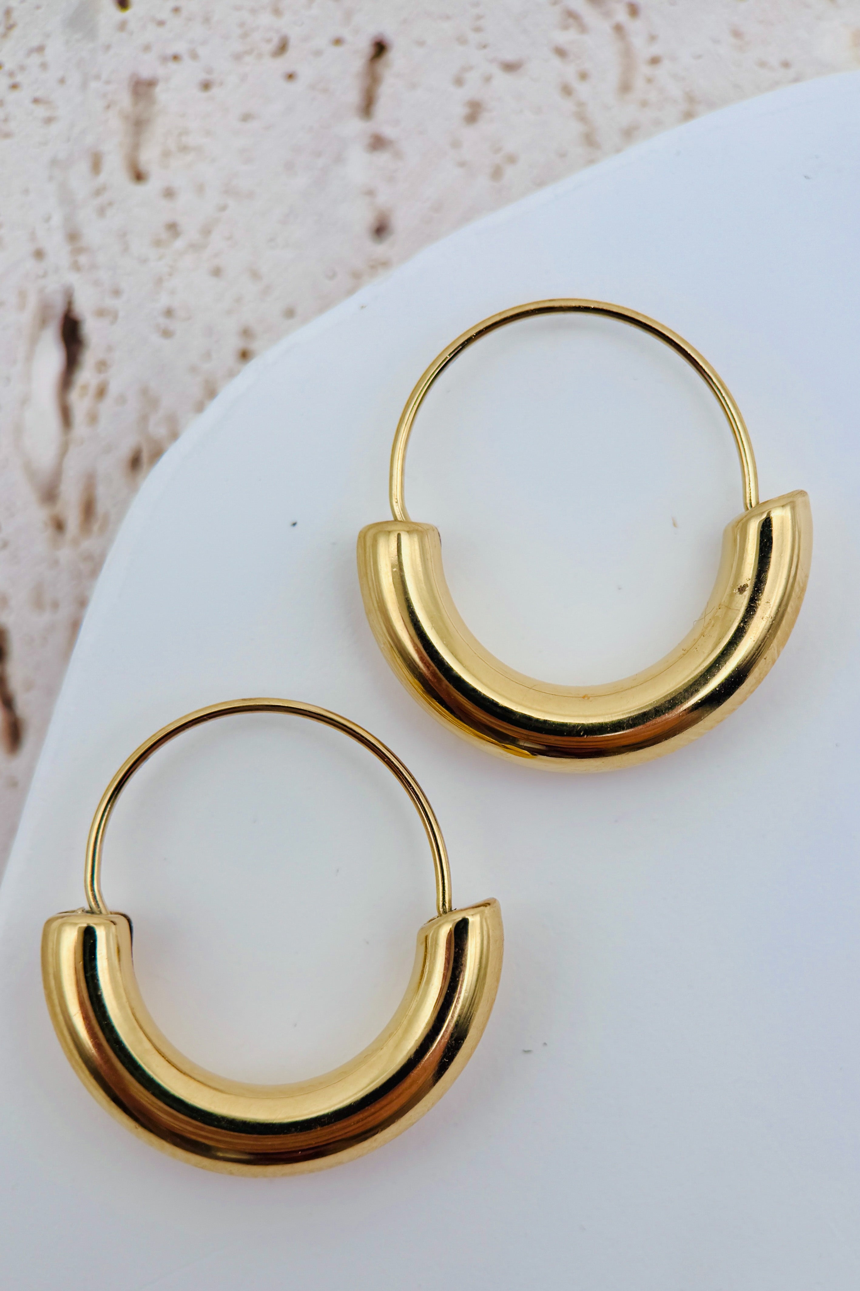 Gold hoop earrings on a white surface with a beige background