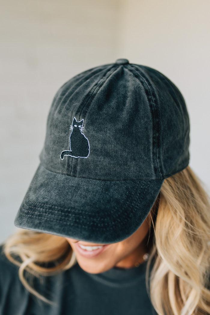 Person wearing a dark gray cap with a cat emblem on a neutral background