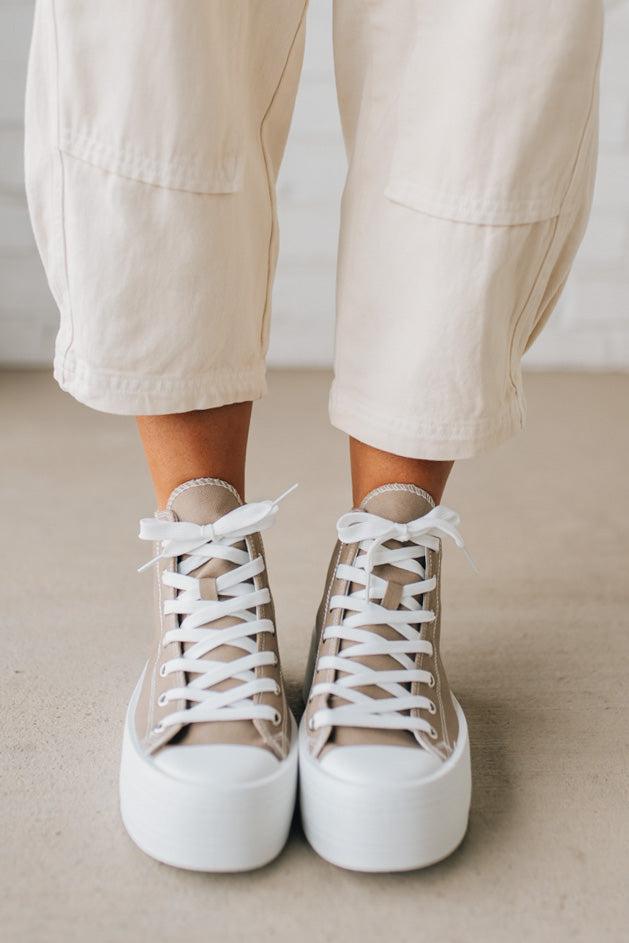 Person wearing beige high-top sneakers with white laces on a neutral background
