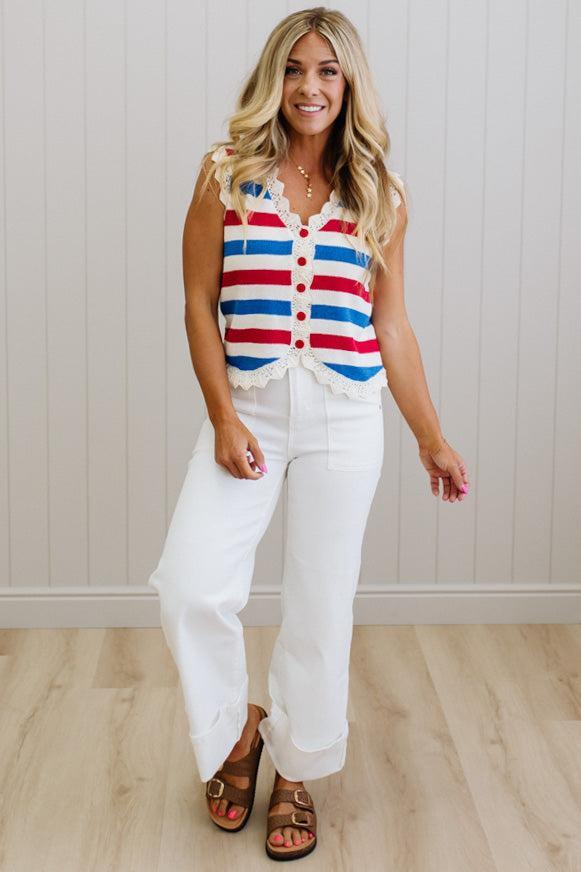 Woman wearing a red, white, and blue striped sleeveless top with white pants against a light wooden panel background.