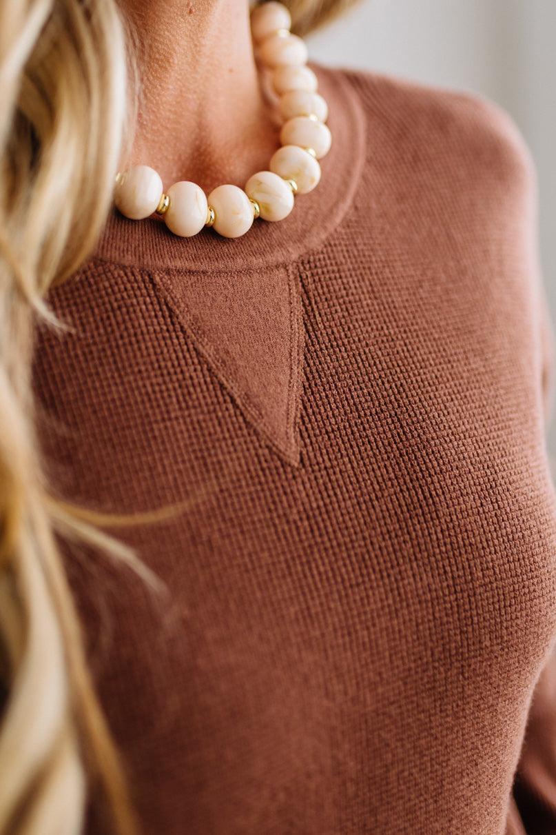 Blonde woman in a plaid hat wearing a solid waffle texture sweater with drop shoulder seams and crewneck.
