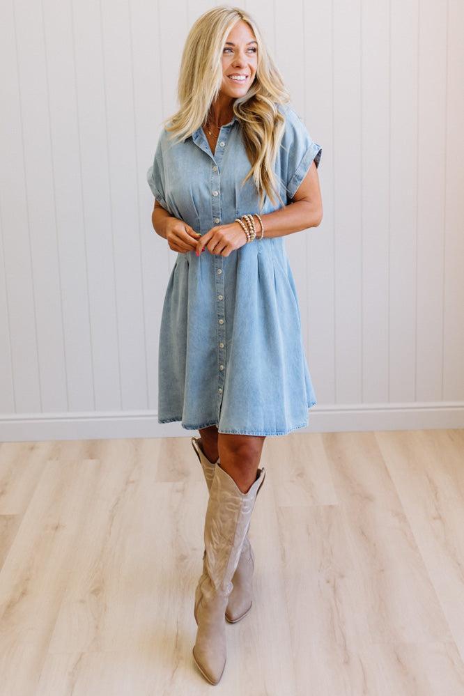 Woman wearing a light blue denim dress and beige knee-high boots indoors.