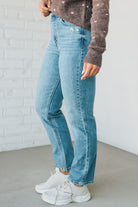 Person wearing blue jeans and a brown sweater against a white brick wall.