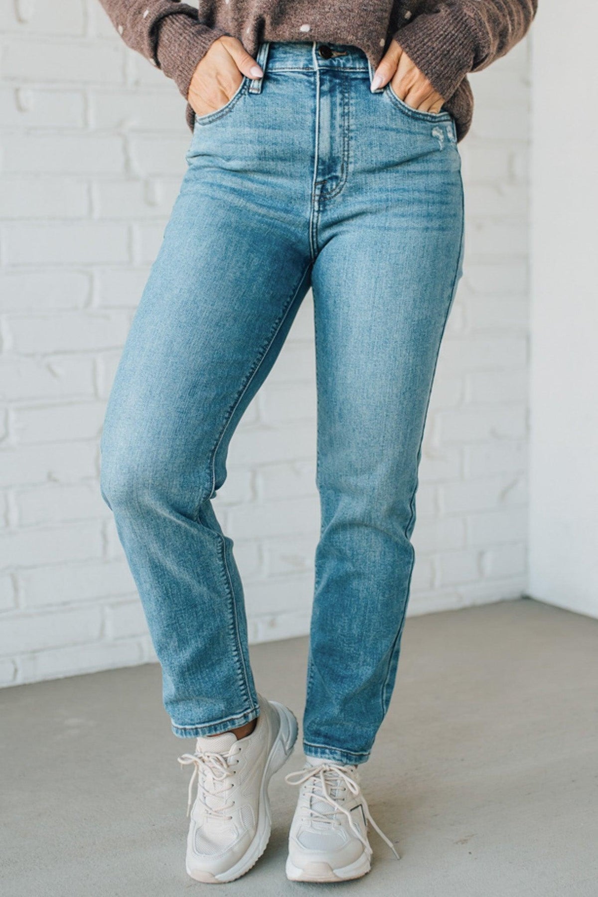 Person wearing blue jeans and white sneakers against a white brick wall.