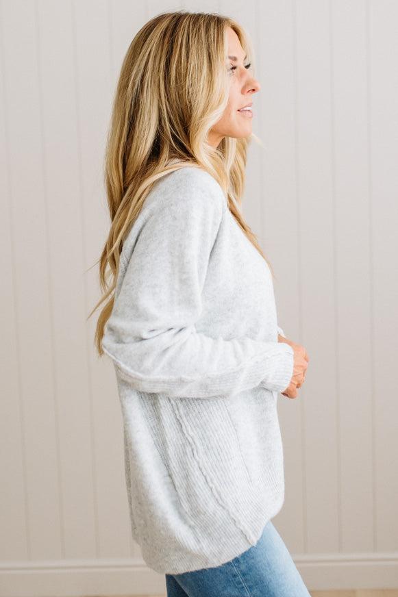BLONDE WOMAN WEARING A HIGH-LOW HEM, LONG SLEEVE, SUPER SOFT, OVERSIZED CREW NECK SWEATER WITH RIB DETAILS AND STANDING IN A STUDIO WITH LIGHT WOOD FLOOR AND PANELED WALL BEHIND.