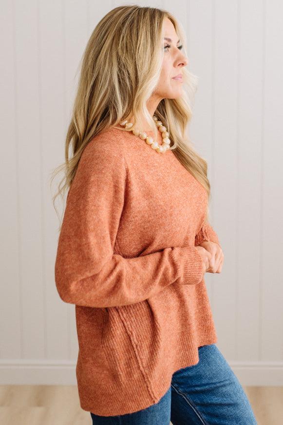 BLONDE WOMAN WEARING A HIGH-LOW HEM, LONG SLEEVE, SUPER SOFT, OVERSIZED CREW NECK SWEATER WITH RIB DETAILS AND STANDING IN A STUDIO WITH LIGHT WOOD FLOOR AND PANELED WALL BEHIND.