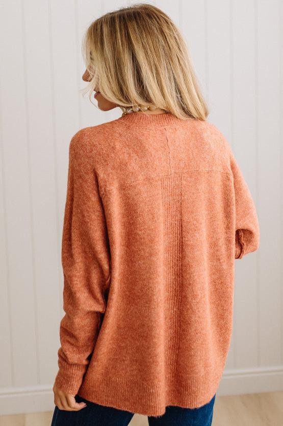 BLONDE WOMAN WEARING A HIGH-LOW HEM, LONG SLEEVE, SUPER SOFT, OVERSIZED CREW NECK SWEATER WITH RIB DETAILS AND STANDING IN A STUDIO WITH LIGHT WOOD FLOOR AND PANELED WALL BEHIND.