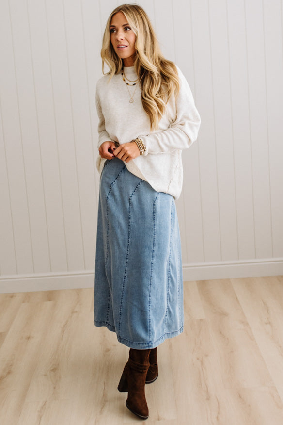 Blonde woman in a studio with light floor and a paneled wall behind, wearing a Denim Diagonal Line Detail Midi Skirt.