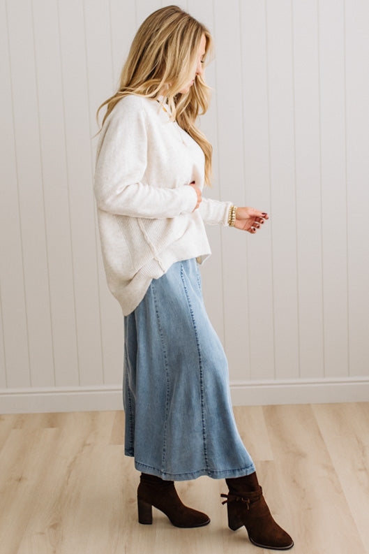Blonde woman in a studio with light floor and a paneled wall behind, wearing a Denim Diagonal Line Detail Midi Skirt.