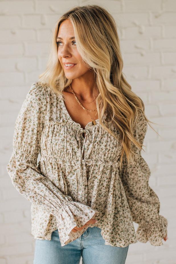 Woman wearing a floral blouse and jeans against a white brick wall
