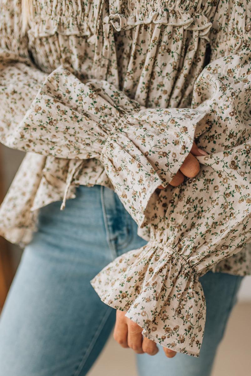 Close-up of a floral blouse with ruffled sleeves and blue jeans.