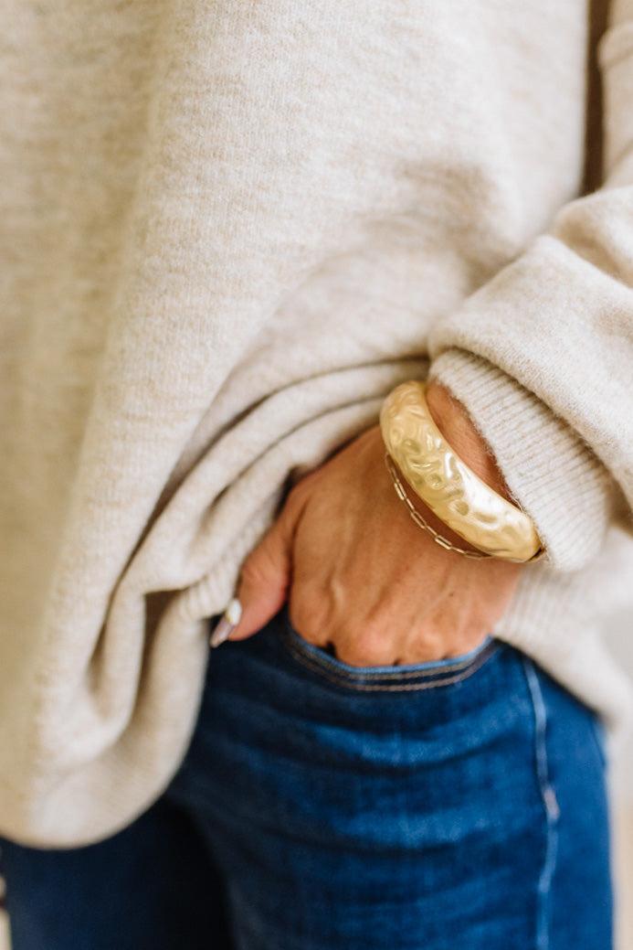 Woman in striped top and light jeans with her hand an a pocket and focused on a large gold bangle.