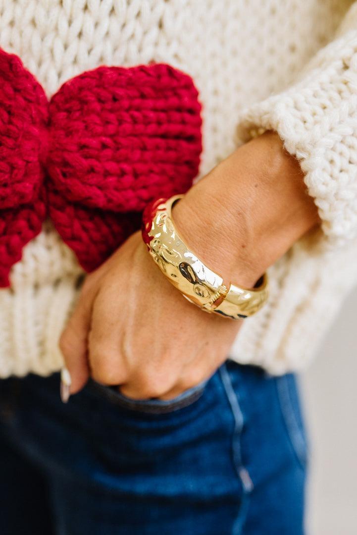 Woman in striped top and light jeans with her hand an a pocket and focused on a large matte gold bangle.