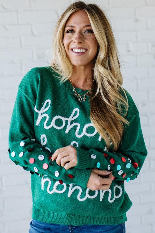 Woman wearing a green sweater with 'ho ho ho' text against a white brick wall.