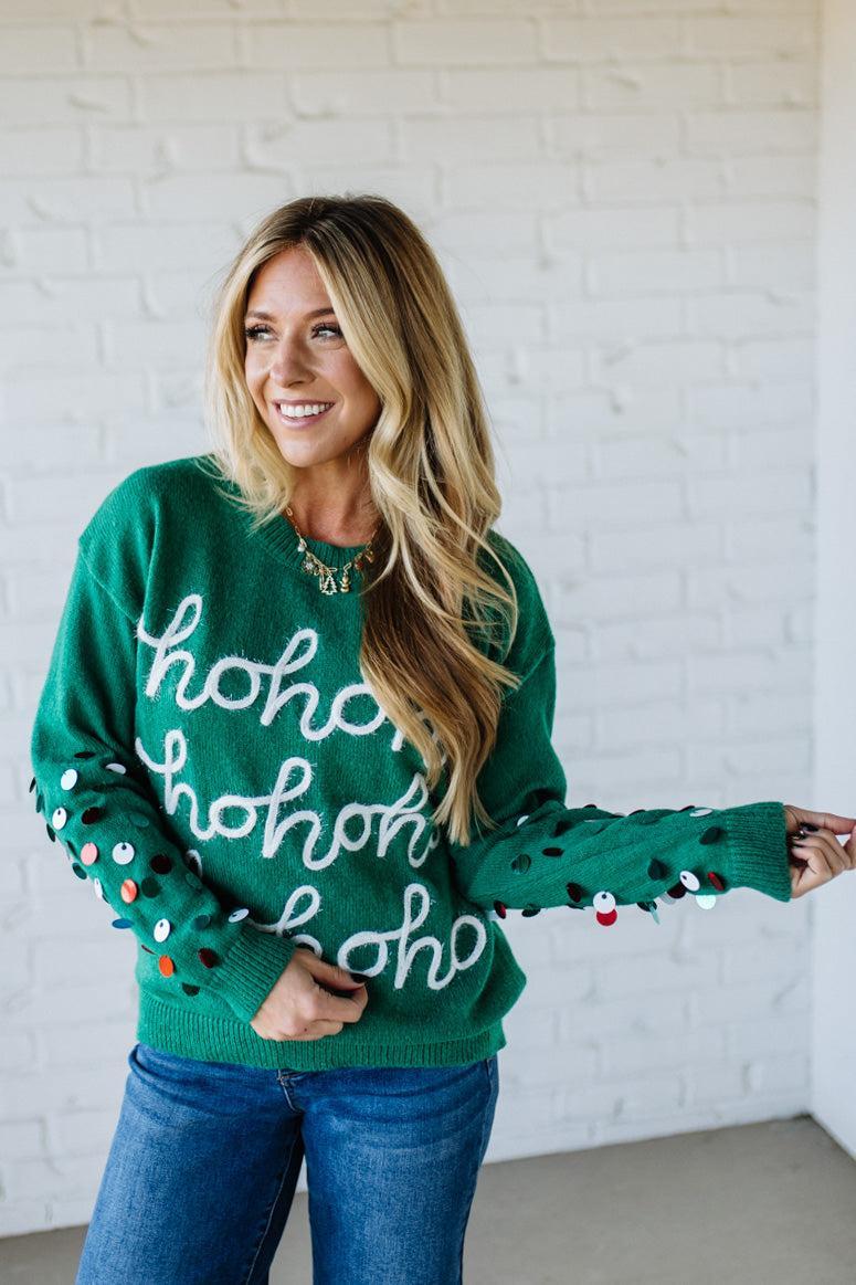 Woman wearing a green sweater with 'ho ho ho' text against a white brick wall.