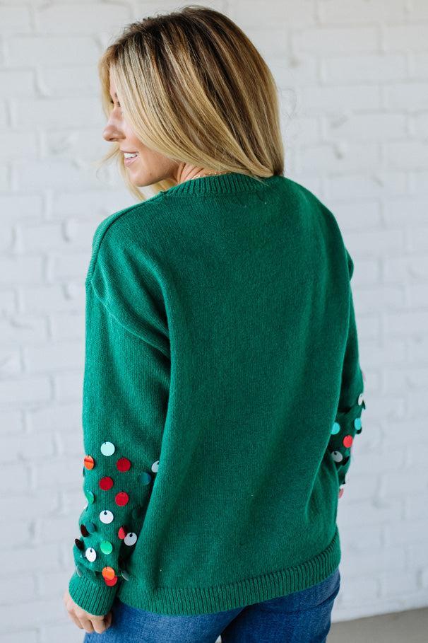 Person wearing a green sweater with colorful buttons on a white brick wall background