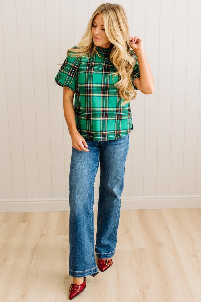 Woman wearing a green plaid top and blue jeans indoors.