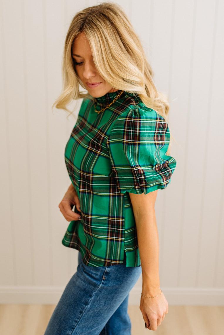 Woman wearing a green plaid shirt and blue jeans against a plain background