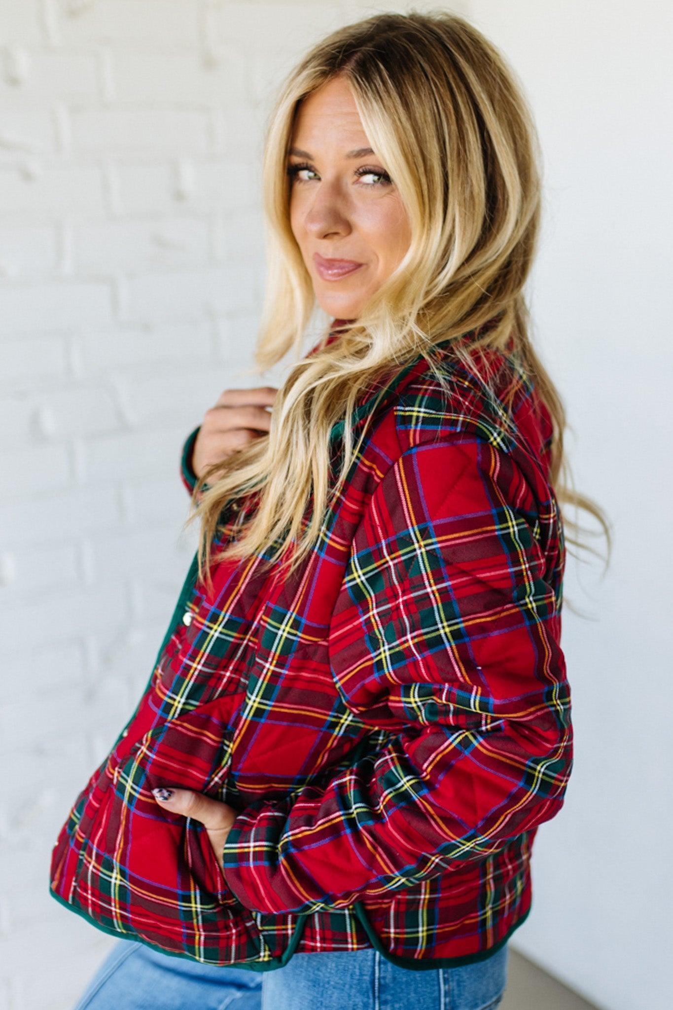 Woman wearing a red plaid jacket against a white brick wall.