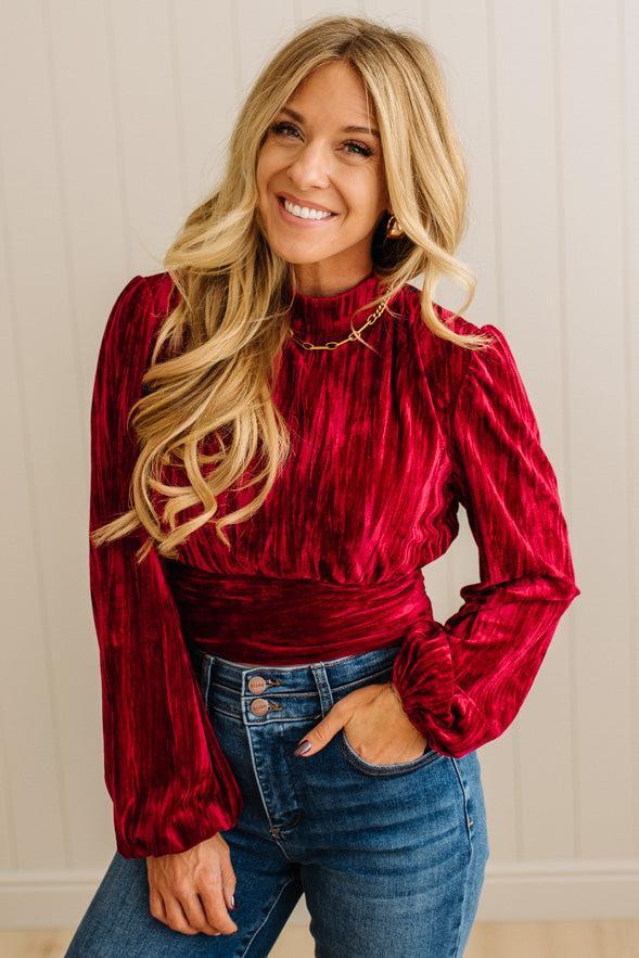 Woman wearing a red velvet top and blue jeans against a neutral background