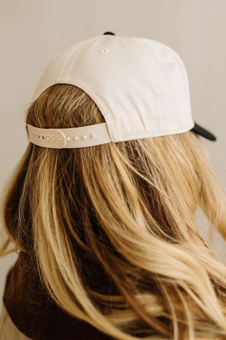 White cap worn by a person with blonde hair on a neutral background