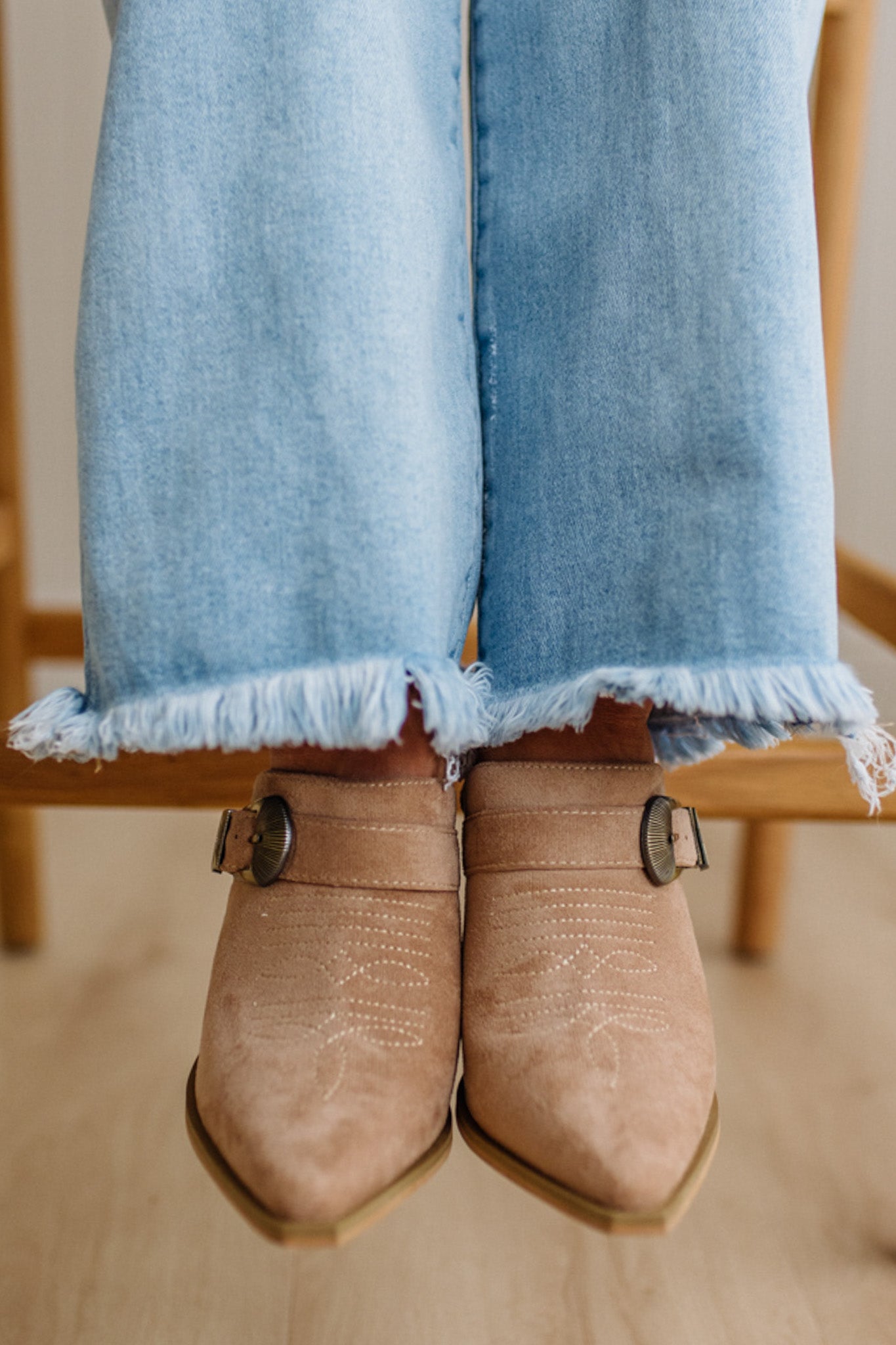 Person wearing light blue jeans and brown shoes with a wooden floor background