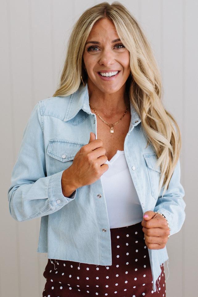 Woman wearing a light blue denim jacket over a white top and polka dot skirt, smiling.