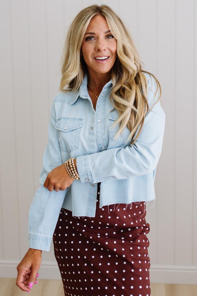 Woman wearing a light blue denim jacket and maroon polka dot skirt indoors.