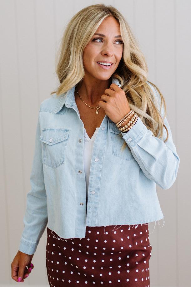 Woman wearing a light blue denim jacket over a white top and maroon skirt with white polka dots.