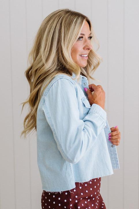 Woman wearing a light blue denim jacket over a red polka dot dress against a plain background