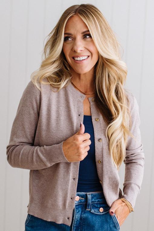 Blonde woman in dark jeans modeling in bright studio wearing a heather mocha cardigan with brown button front.
