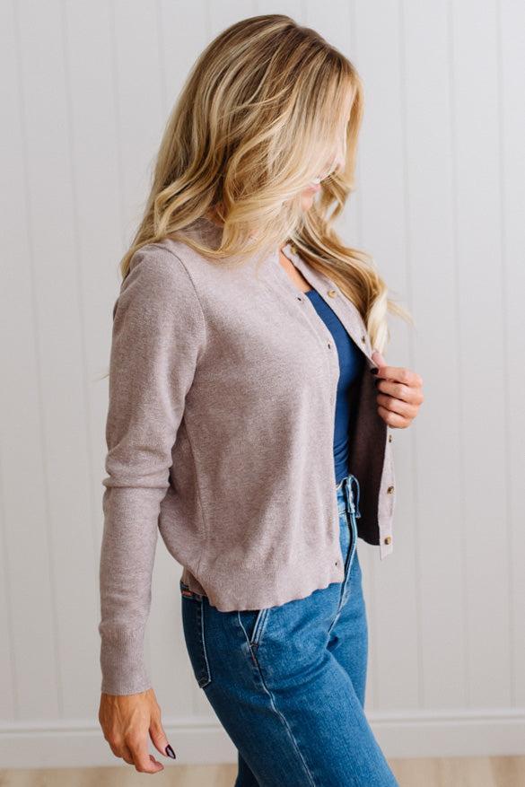 Blonde woman in dark jeans modeling in bright studio wearing a heather mocha cardigan with brown button front.