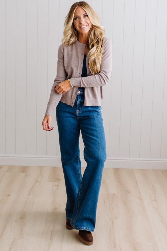 Blonde woman in dark jeans modeling in bright studio wearing a heather mocha cardigan with brown button front.
